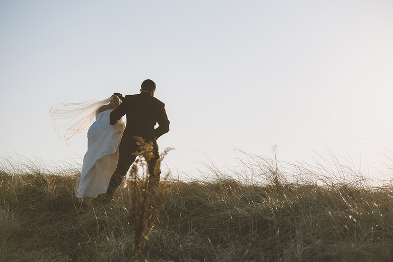 bride and groom climb sand dune